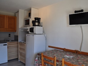 A compact kitchen with a microwave, coffee maker, and refrigerator. There is a bed with a patterned blanket and wooden headboard. - Charming flat near village with parking (Châtel)
