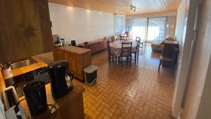 A spacious living area with a wooden ceiling, a dining table with chairs, a sofa, and a TV.