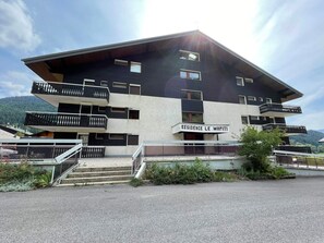 A multi-story building with balconies, a sign reading "RESIDENCE LE WAPITI," and a mountainous backdrop.