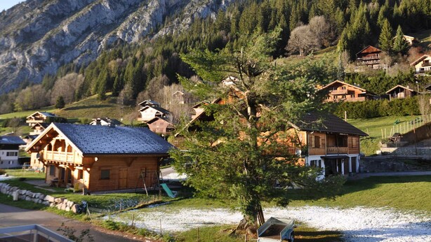 A mountain village with wooden houses, a playground, and a clear view of the surrounding mountains.