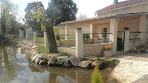 A riverside building with a stone wall, a small garden with flowers, and a green gate.