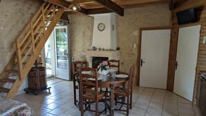 A rustic dining area with a wooden table, chairs, and a fireplace. A wooden staircase leads to an outdoor area.
