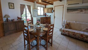 A cozy dining area with a wooden table and chairs, a kitchen in the background, and a sofa with a floral pattern.