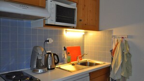 A kitchen with a microwave, kettle, and stove, wooden cabinets, and a tiled backsplash. - Apartment with terrace, ski locker and covered parking (Châtel)