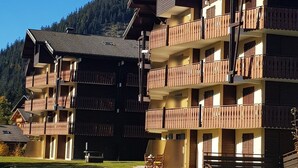 A multi-story hotel with balconies, a ski slope in the background, and a clear sky. - Apartment with terrace, ski locker and covered parking (Châtel)