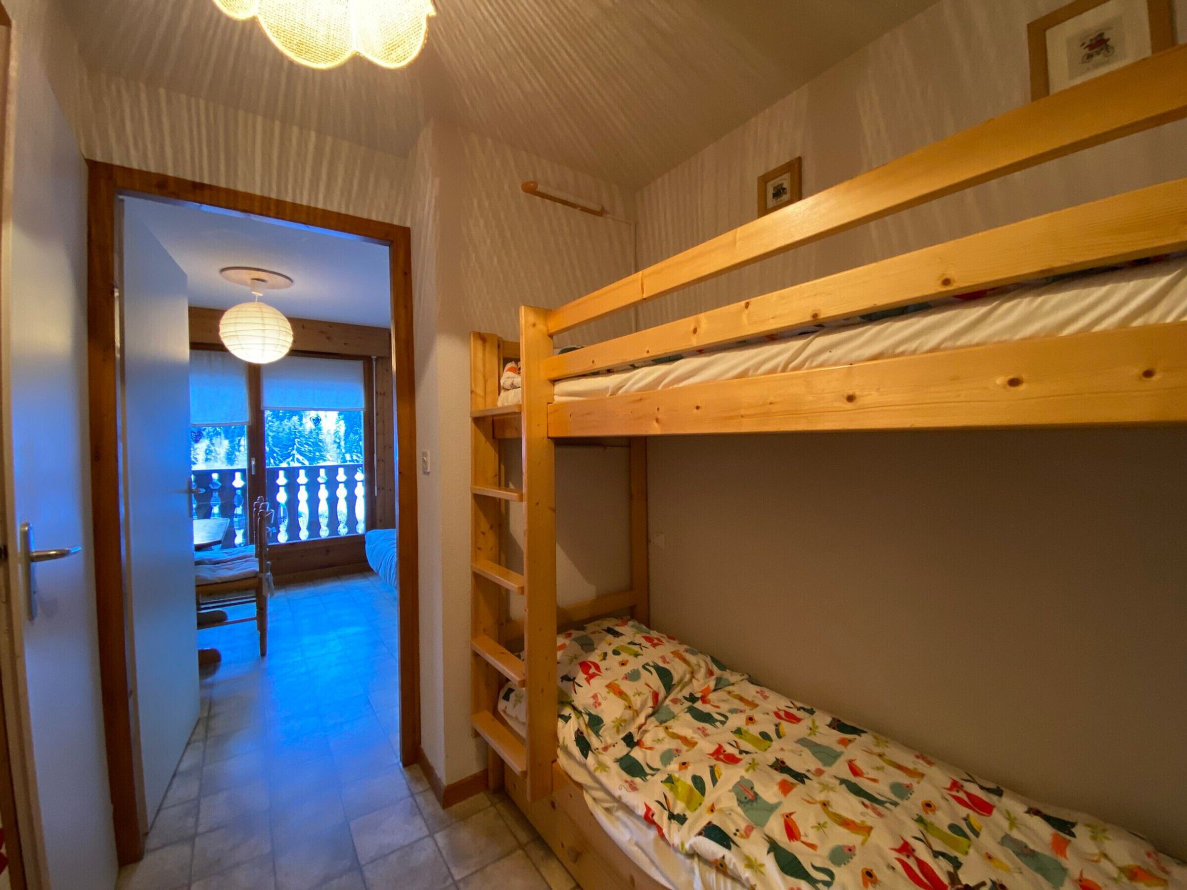 A room with a bunk bed, a wooden shelf unit, and a view through an open door to a balcony.