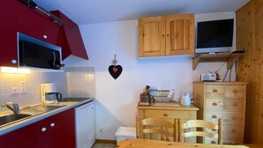A compact kitchen with red cabinets, a microwave, a coffee maker, and a wooden table. - Quiet studio with balcony and parking near Châtel center (Châtel)