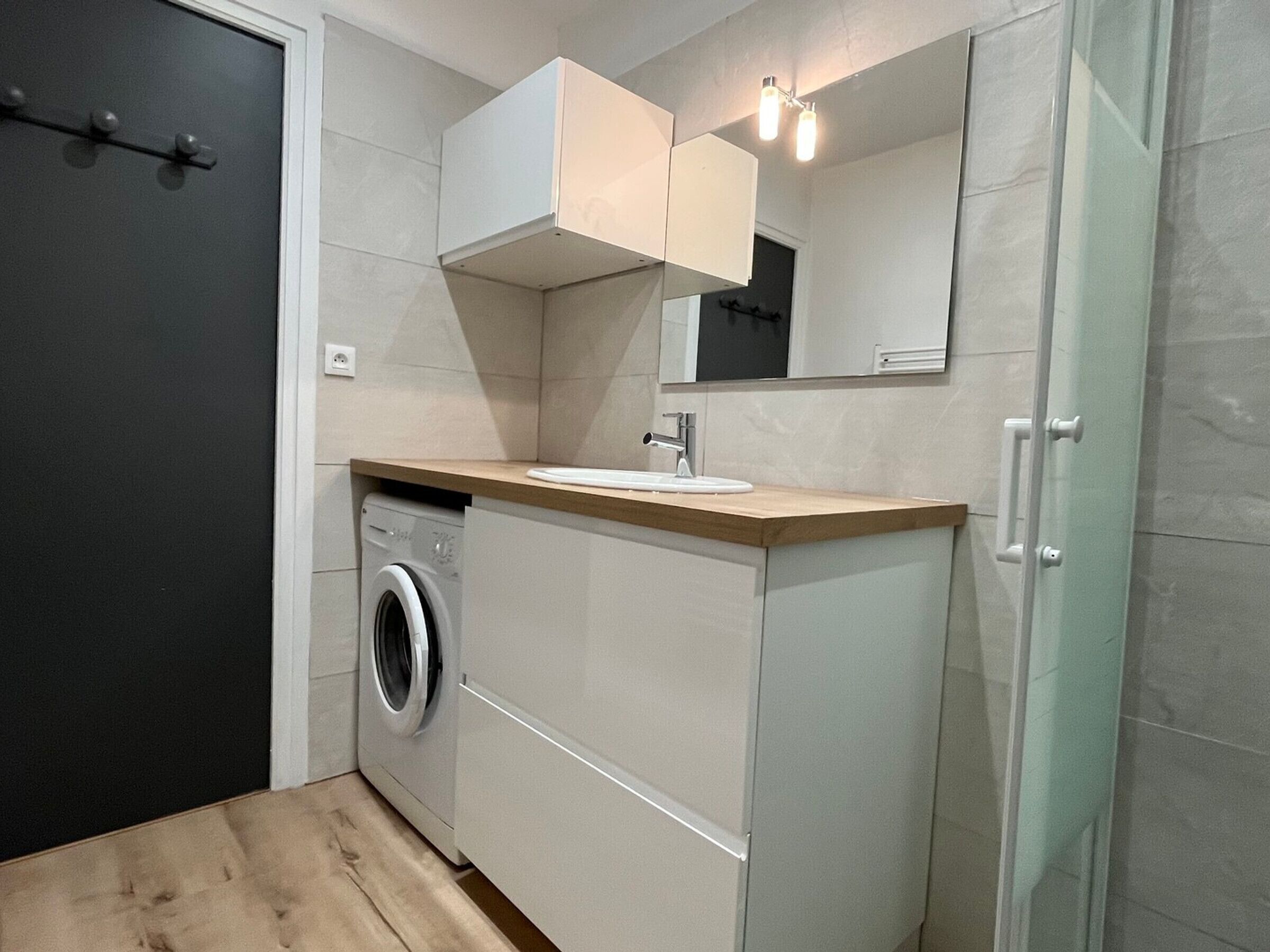 Une petite salle de bain équipée d’un lave-linge, d’un lavabo et d’un miroir.