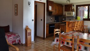 A compact kitchen with wooden cabinets, a dining table with chairs, and a small refrigerator. - Spacious apartment in Châtel with sunny terrace (Châtel)