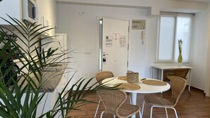 Un comedor con una mesa redonda, sillas de mimbre, una planta en maceta y una zona de cocina con microondas.