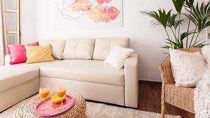 Una sala de estar moderna con un sofá color beige, un sillón de mimbre y una planta grande en maceta.