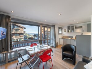 Una habitación de hotel moderna con comedor, cocina y balcón con vistas a la montaña.