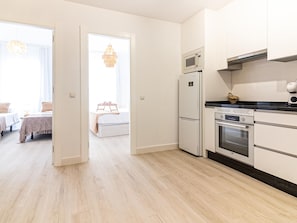 A modern kitchen with a microwave, oven, and refrigerator. There is a dining area with a table and chairs visible through an open door.