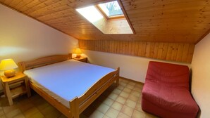 A bedroom with a wooden ceiling, a skylight, a bed, a nightstand with a lamp, and a red chair. - Cozy apartment near the center, pets allowed (Châtel)
