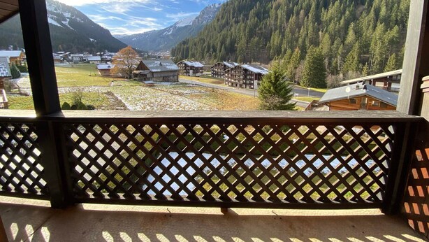 A wooden balcony with a lattice railing overlooking a mountainous landscape with buildings and a clear sky. - Cozy apartment near the center, pets allowed (Châtel)