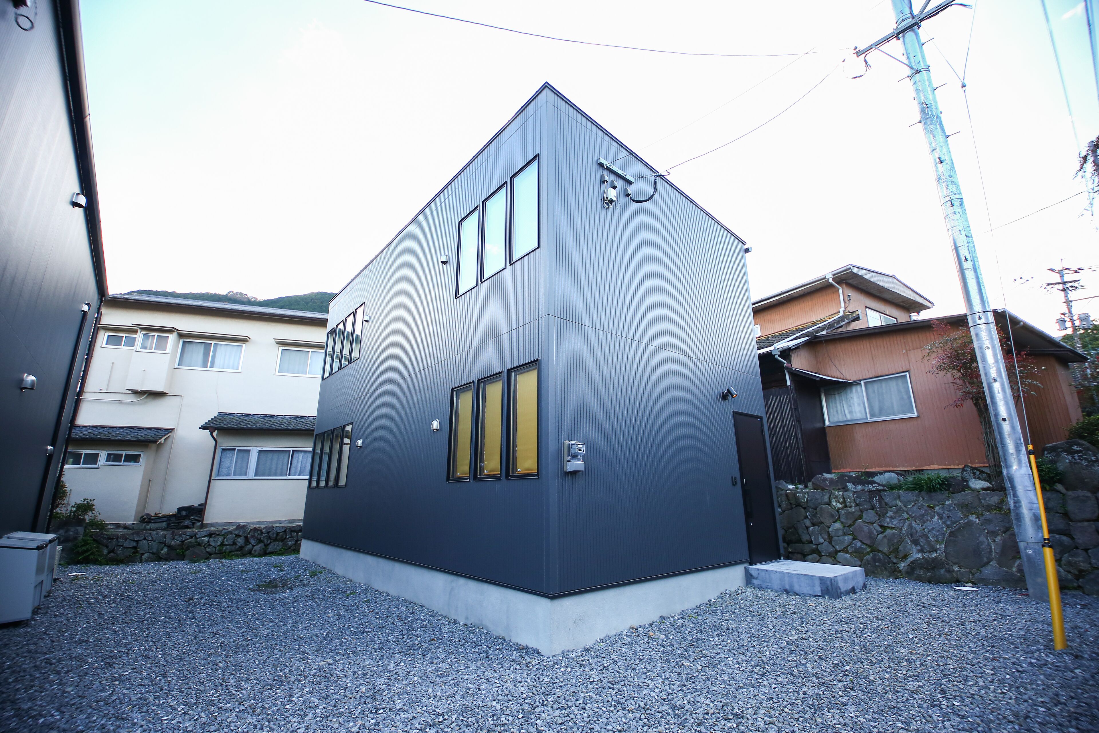 A modern building with a dark facade, multiple windows, and a stone wall.