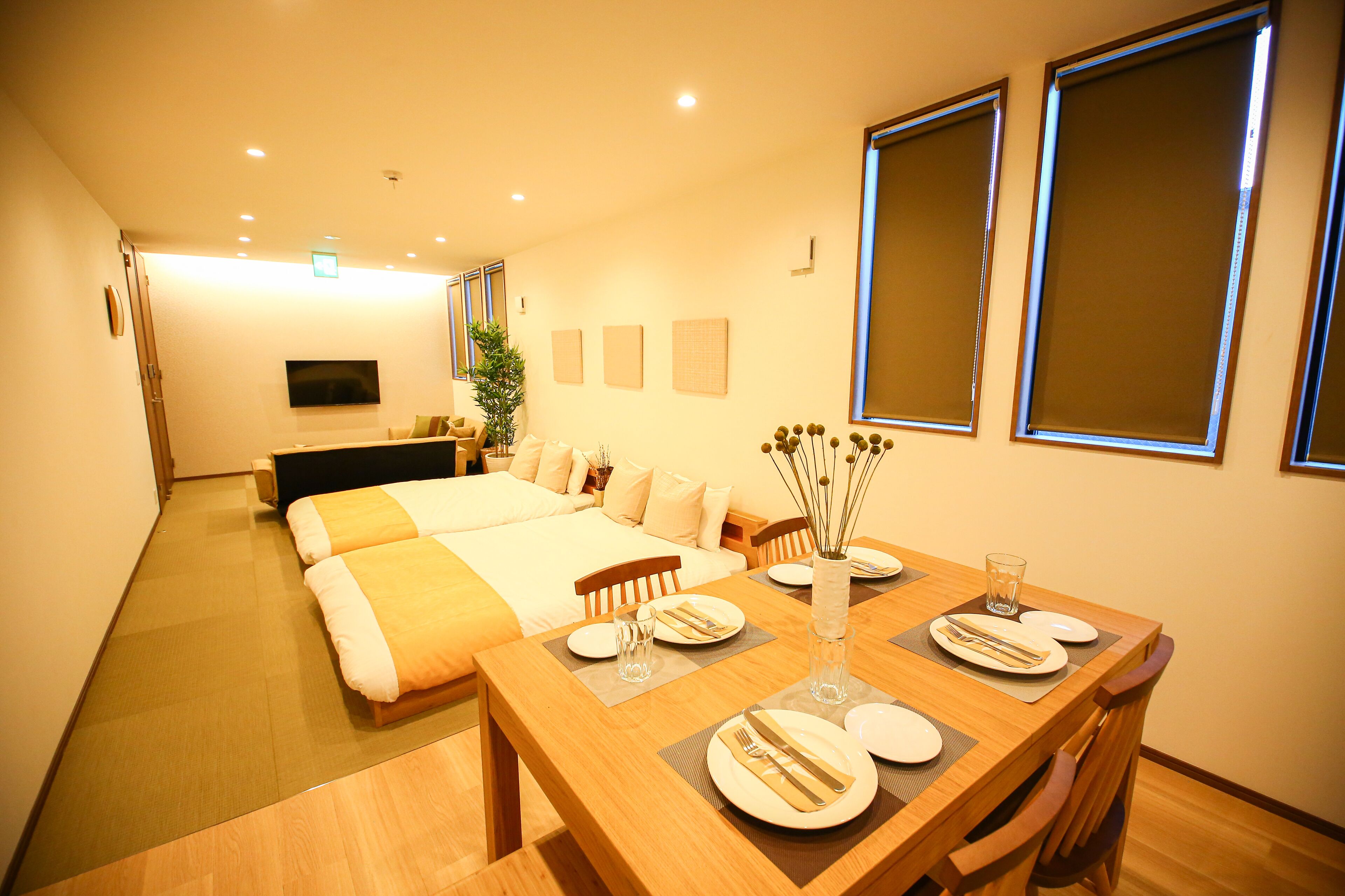 Una habitación de hotel con una cama grande, una mesa de comedor lista para dos personas y un televisor montado en la pared.