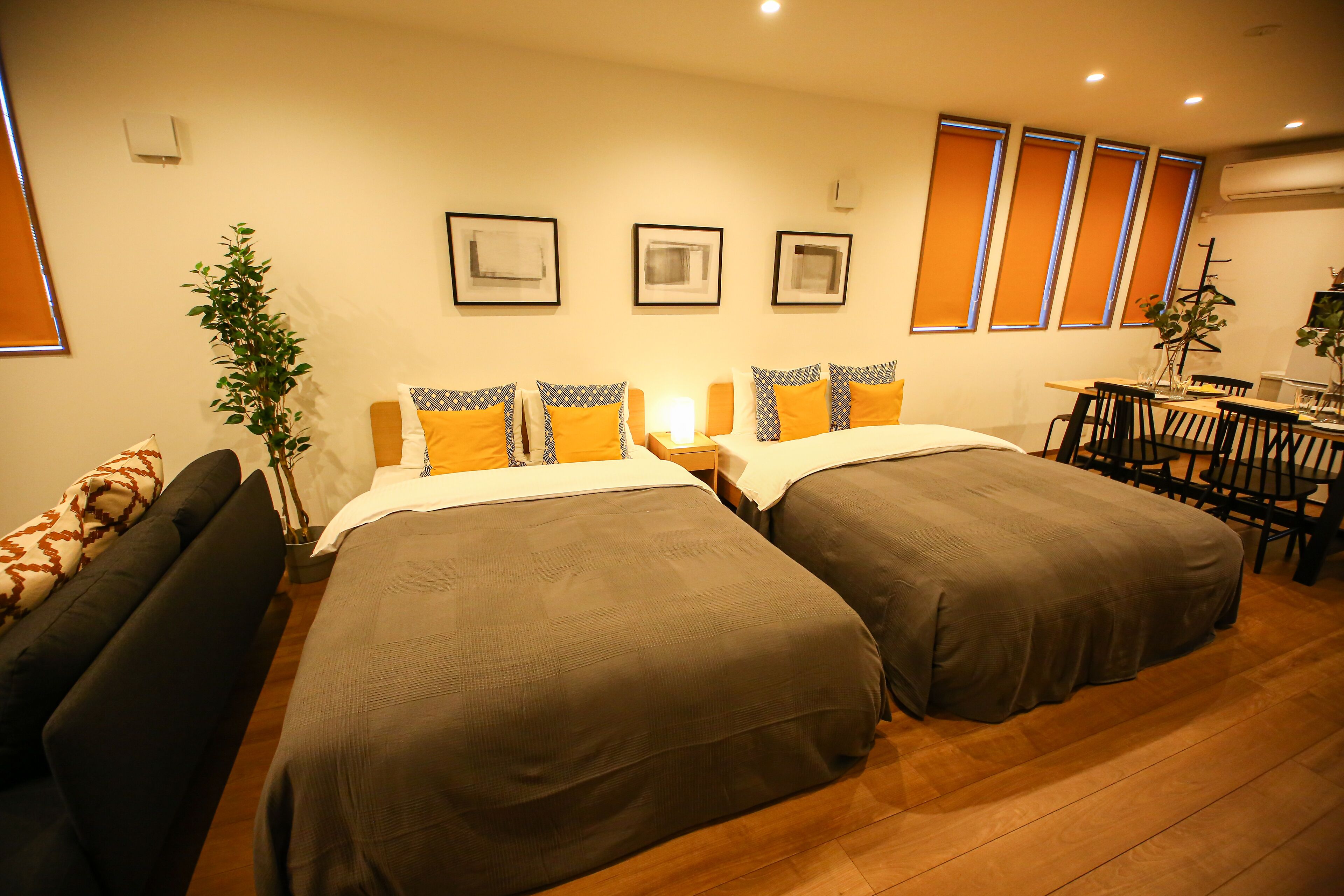 Habitación de hotel con dos camas, una mesa de comedor, sillas, una planta y cuadros en la pared.