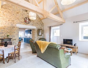 A spacious living area with a stone wall, a green sofa, a dining table with chairs, a television, and a kitchen in the background.