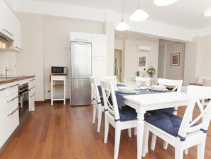 Eine moderne Küche mit weißen Schränken, einem Edelstahlkühlschrank und einem Essbereich mit weißen Stühlen und einer blauen Tischdecke.