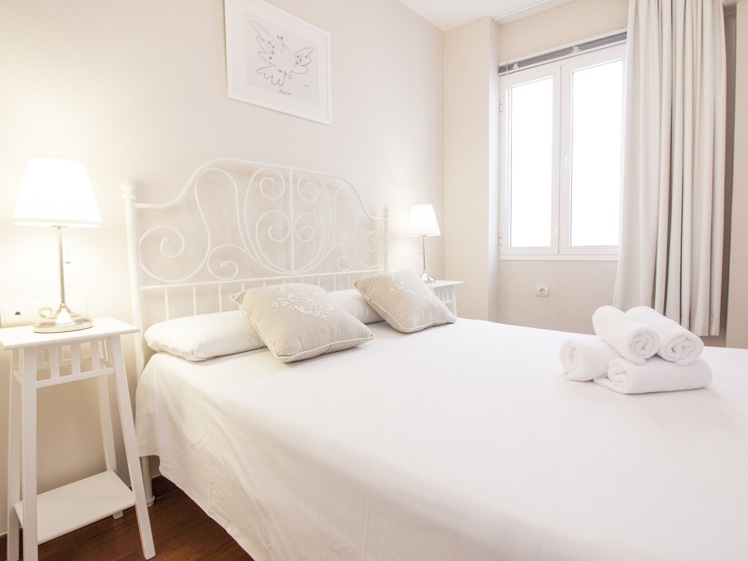 A neatly made bed with pillows, a bedside table with a lamp, and a window with curtains.