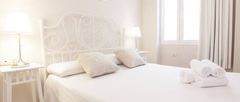 A neatly made bed with pillows, a bedside table with a lamp, and a window with curtains.