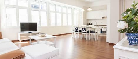 A spacious living area with a dining set, a television, and a kitchen in the background.