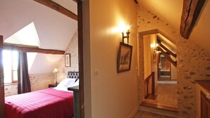 Ein Schlafzimmer mit roter Bettdecke, einem Nachttisch, einer Lampe und einem gerahmten Bild an der Wand.