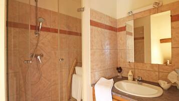 Un baño con ducha de vidrio, lavamanos con espejo y armarios de madera.
