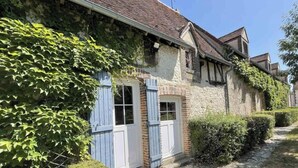 A traditional stone building with a gabled roof, a small front porch, and a pathway leading to the entrance.