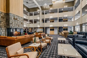 A spacious lobby with a stone fireplace, multiple seating areas, and a high ceiling with lighting fixtures.