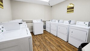 A laundry facility with multiple washing machines and dryers, wooden flooring, and a white ceiling with fluorescent lighting.