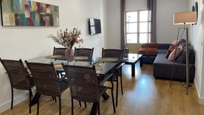 A modern living room with a dining table, wicker chairs, a sofa, and a floor lamp. - Charming Renovated Apartment with Cathedral View in Central Málaga (Málaga)