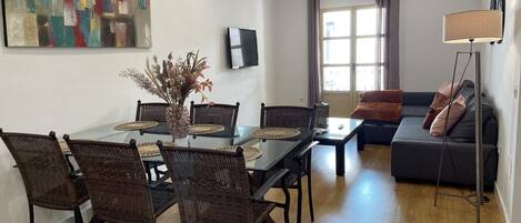 A modern living room with a dining table, wicker chairs, a sofa, and a floor lamp.