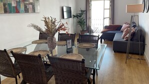 A modern living room with a glass dining table, wicker chairs, a grey sofa, a floor lamp, and a large abstract painting on the wall. - Charming Renovated Apartment with Cathedral View in Central Málaga (Málaga)