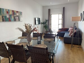 A modern living room with a glass dining table, wicker chairs, a grey sofa, and a floor lamp. - Charming Renovated Apartment with Cathedral View in Central Málaga (Málaga)