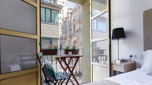 A hotel room with a bed, a desk with a lamp, a chair, a small table with a plant, and a view of the cityscape through the window. - Charming Renovated Apartment with Cathedral View in Central Málaga (Málaga)