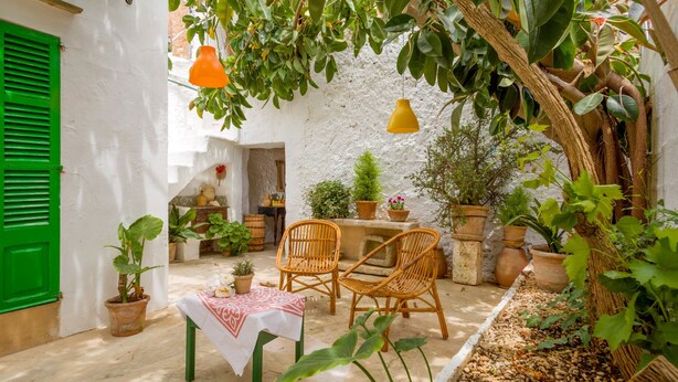 A cozy outdoor seating area with wicker chairs and a table, surrounded by potted plants and a white wall. - Cas Padrins Art i Jardi (Campos)
