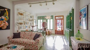 A living room with a floral sofa, a glass coffee table, and a bookshelf filled with books and decorative items. - Cas Padrins Art i Jardi (Campos)
