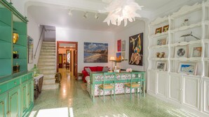 A spacious living room with a staircase, a red sofa, a green table with floral chairs, and a white shelving unit with artwork. - Cas Padrins Art i Jardi (Campos)