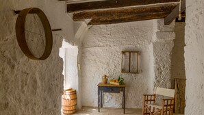 A rustic room with a wooden barrel, a small table with a basket of fruit, a rocking chair, and a wooden cabinet. - Cas Padrins Art i Jardi (Campos)