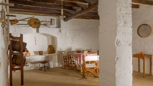 A rustic room with a wooden table, chairs, a small shelf with pottery, and a hanging light fixture. - Cas Padrins Art i Jardi (Campos)