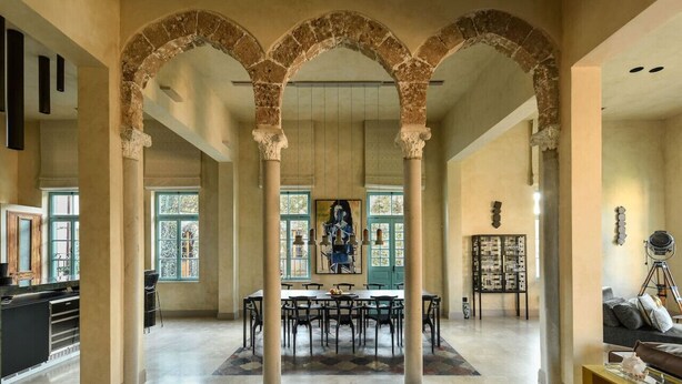Un interior espacioso con zona de comedor central, arcos de piedra y vistas amplias a través de grandes ventanales.