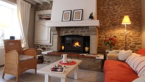 A cozy living room with a stone fireplace, a wicker chair, a white coffee table, and a red sofa. - Spacious house near Cherbourg with enclosed garden and pets allowed (Gonneville-Le Theil)