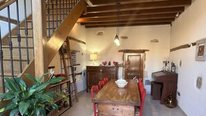 Un comedor con una mesa de madera y sillas rojas, una escalera con barandilla de metal y una lámpara colgante.