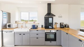 Een moderne keuken met grijze kasten, een zwarte afzuigkap, een magnetron, een spoelbak, een vaatwasser en een raam met uitzicht op het landschap.