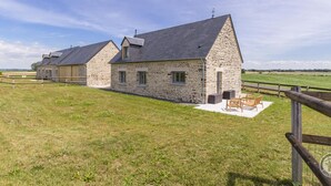 Een stenen boerderij met schuin dak, een omheind erf en terras.