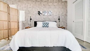 A bedroom with a large bed, wooden wardrobe, and a concrete textured wall.