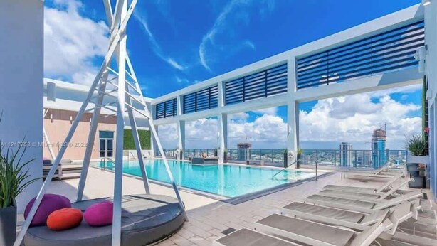 Ein Poolbereich auf dem Dach mit freiem Blick auf die Stadtlandschaft, Liegestühle und eine kleine Spielanlage.