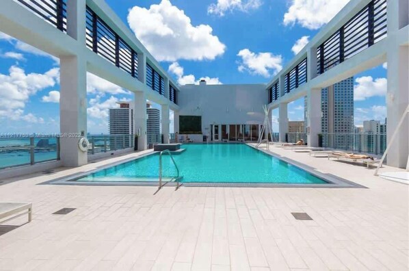 A rooftop pool with a clear view of the city skyline, surrounded by white pillars and a glass railing.